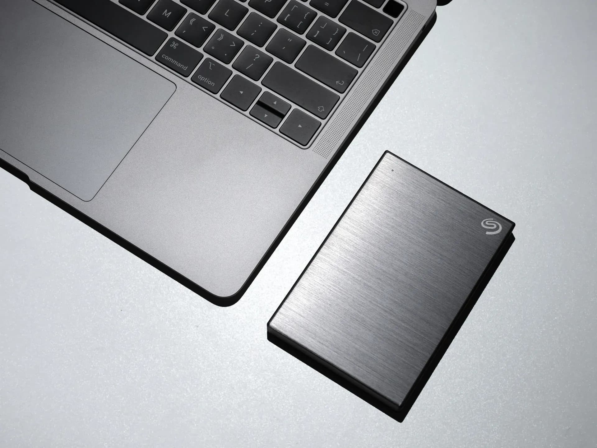 Laptop e disco esterno appoggiati su una scrivania chiara