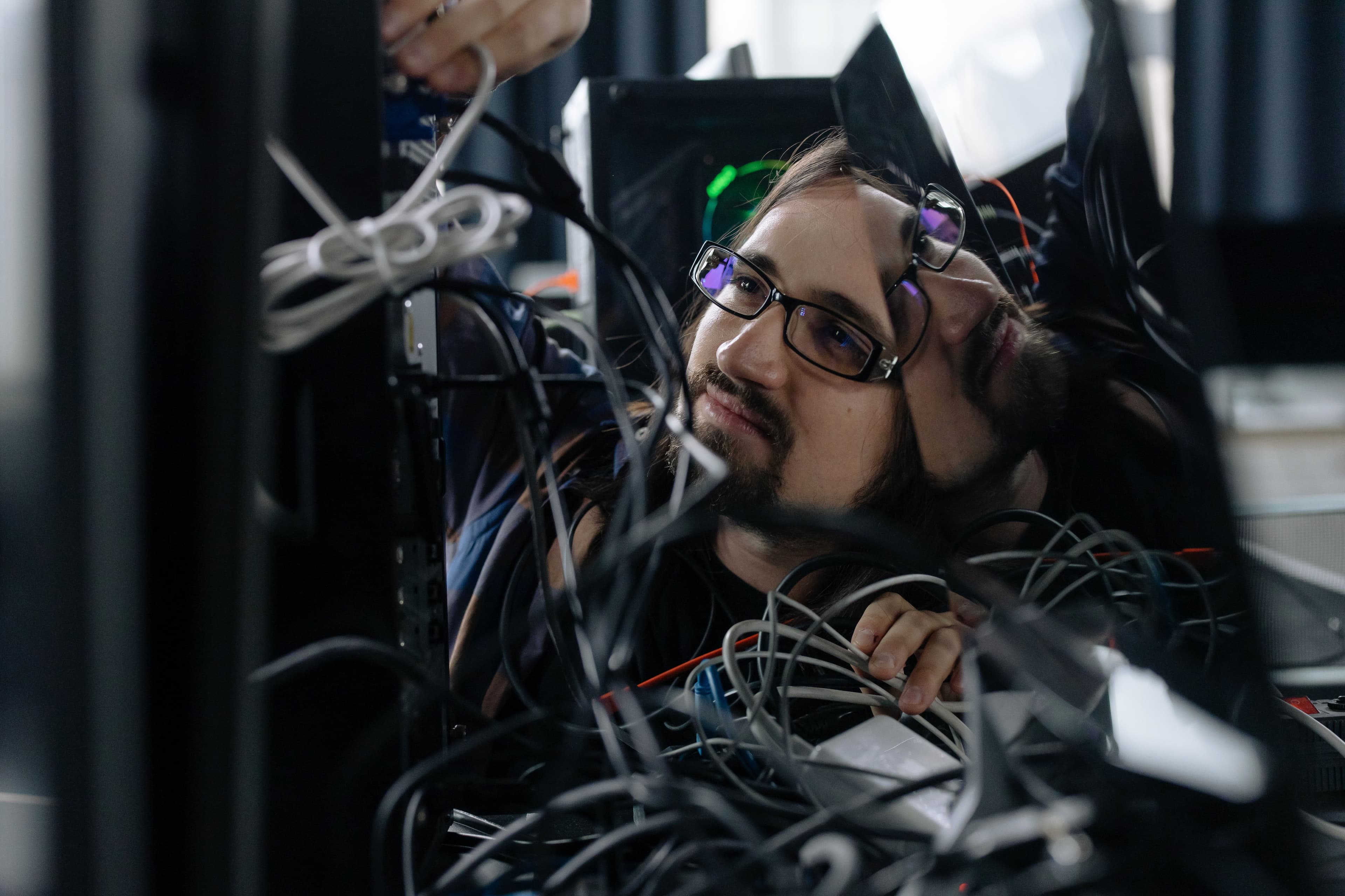 Tecnico con gli occhiali al lavoro fra i cavi di un armadio di rete